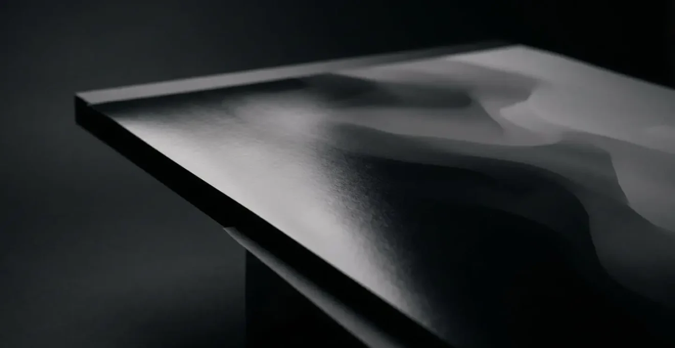 Dramatic side-lit view of glossy photographic print showing uniform surface sheen and deep black density without visible text