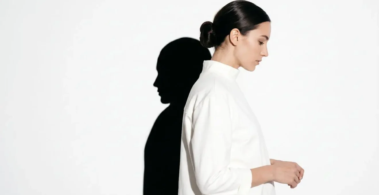 Symbolic composition showing one deliberate hard shadow in otherwise bright high-key scene creating visual tension